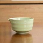 A pale green ceramic pitcher with a small spout from the "Zielony zestaw do matchy 4 elementy" sits on wood, its smooth, ridged design evoking the elegance of traditional akcesoria do herbaty.